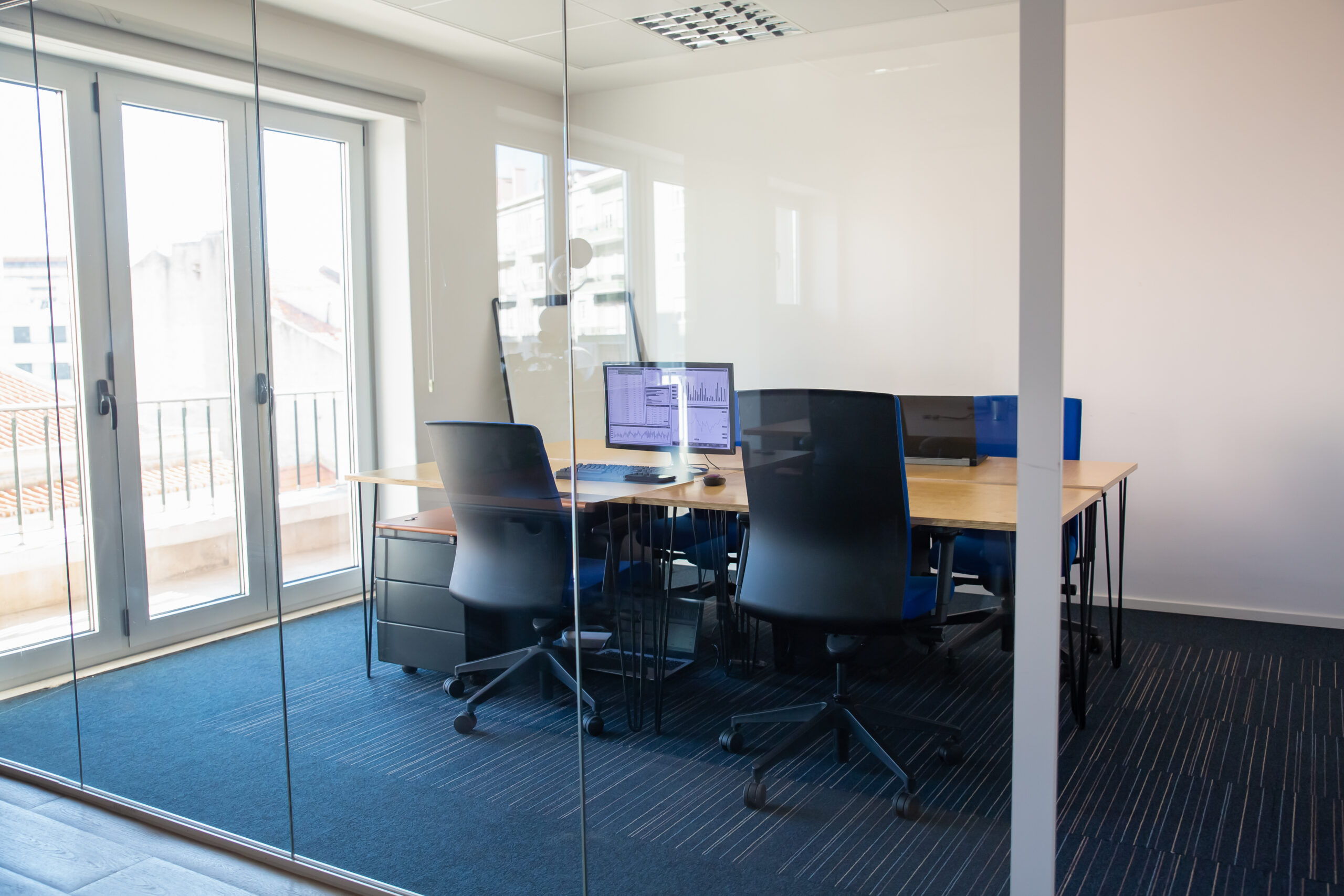 empty-boardroom-behind-glass-wall-meeting-room-with-conference-table-shared-desk-for-team-and-workplaces-trading-graphs-on-monitor-office-interior-or-commercial-real-estate-concept-scaled.jpg