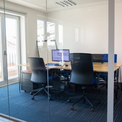 empty-boardroom-behind-glass-wall-meeting-room-with-conference-table-shared-desk-for-team-and-workplaces-trading-graphs-on-monitor-office-interior-or-commercial-real-estate-concept-scaled.jpg